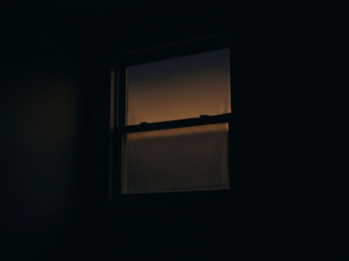 Una ventana a oscuras al amanecer, con el cielo apenas empezando a encenderse.